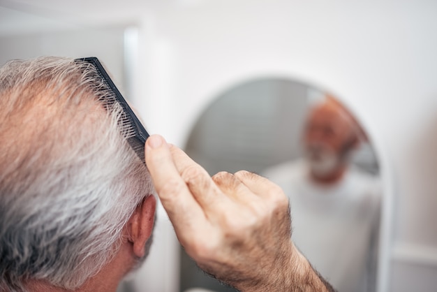 Hogere mens het borstelen haar in badkamers, close-up.