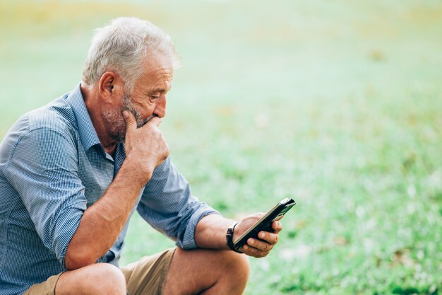 Hogere mensen die een smartphone gebruiken terwijl het zitten op gras in het park