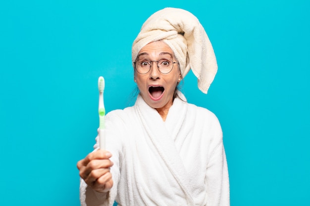 Hogere Mooie vrouw die na het douchen een badjas draagt en met een tandenborstel