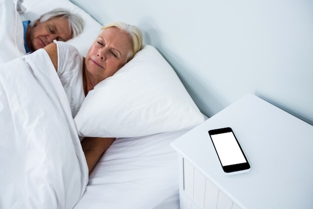 Hogere paarslaap op bed met telefoon op lijst