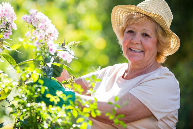 Hogere vrouw die bloemen in tuin onderzoekt