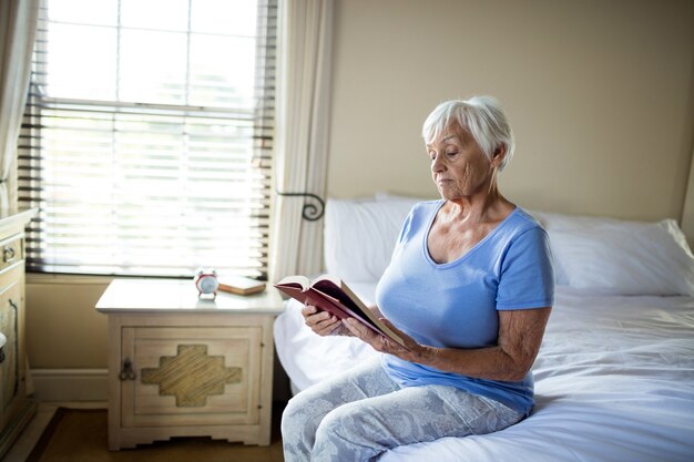 Hogere vrouw die een boek in de slaapkamer thuis leest