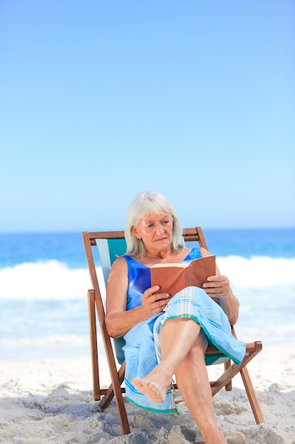 Hogere vrouw die een boek op het strand leest