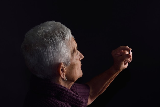 Hogere vrouw die een pil met grijze achtergrond kijkt