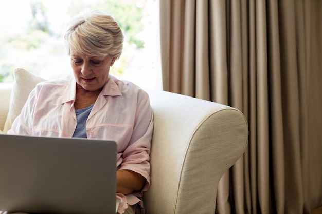 Hogere vrouw die laptop in woonkamer met behulp van