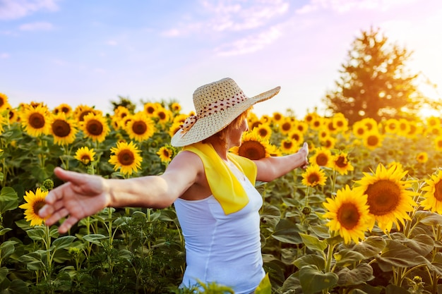 Hogere vrouw die op bloeiend zonnebloemgebied lopen die vrij en bewonderend mening voelen. Zomervakantie