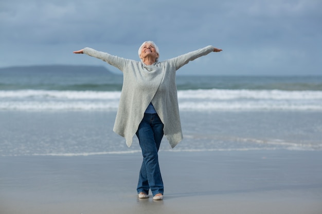 Hogere vrouw die uitrekkende oefening op het strand doet