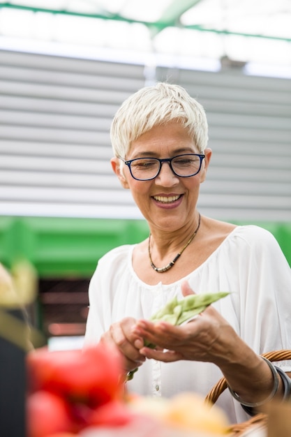 Hogere vrouw die verse organische groente op markt kopen