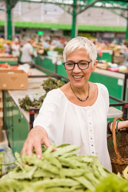 Hogere vrouw die verse organische groente op markt kopen