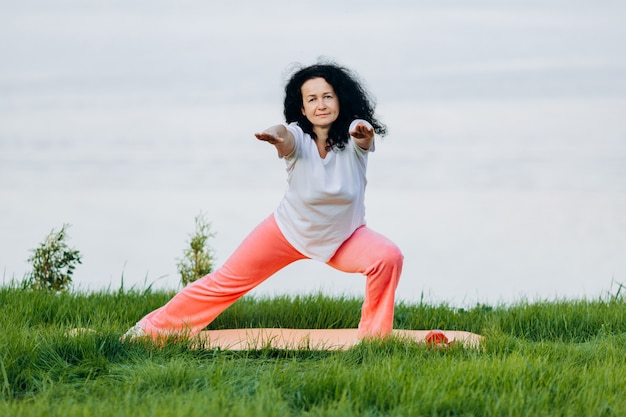 Hogere vrouw die yogaasana met rechte en handen doet openlucht kijkt. vooraanzicht