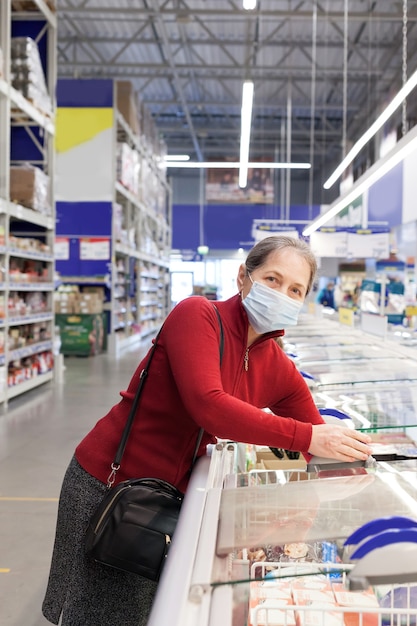 Hogere vrouwelijke klant in supermarkt die beschermend medisch masker draagt