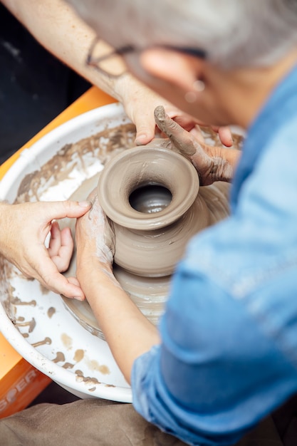 Hogere vrouwelijke pottenbakker die aan aardewerkwiel werken terwijl het zitten in haar workshop