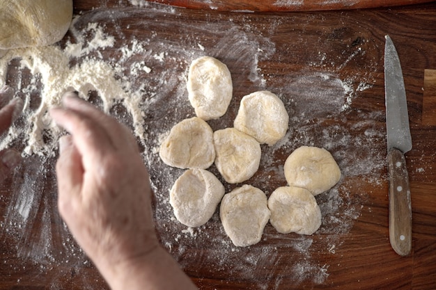 Hogere vrouwenhanden die deeg in bloem met deegroller uitrollen in haar huiskeuken