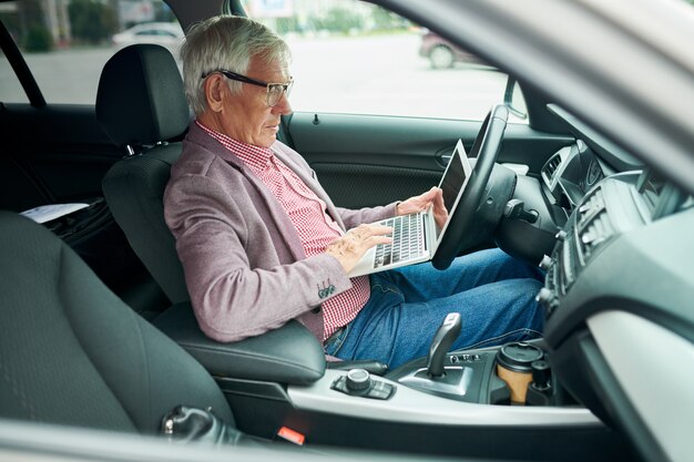 Hogere zakenman die laptop in auto met behulp van