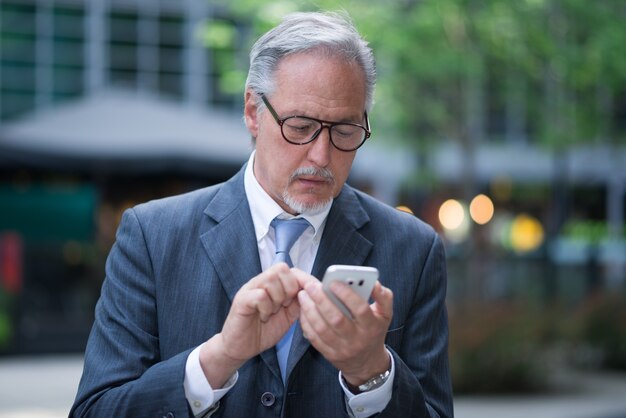 Hogere zakenman die zijn mobiele telefoon in openlucht met behulp van