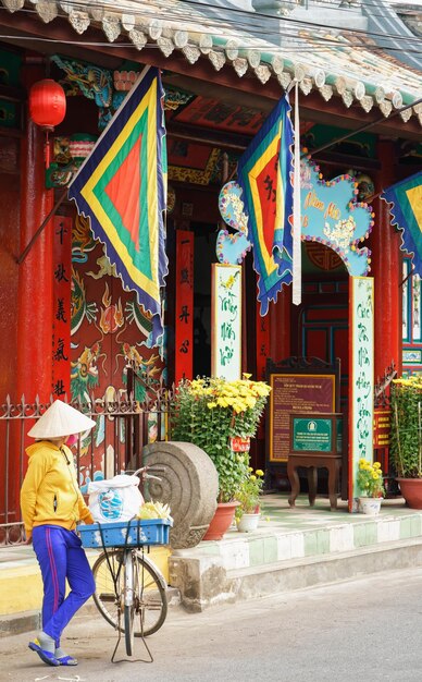 Hoi An, Vietnam - 16 februari 2016: Aziatische vrouw in een traditionele hoed en met een fiets verkoopt voedsel op straat in Hoi An, Vietnam.