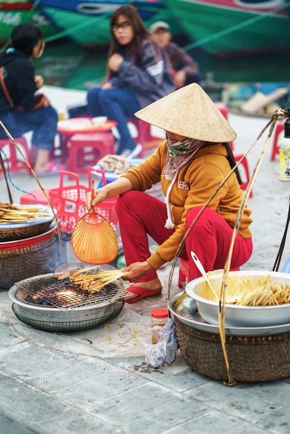 Hoi An, Vietnam - February 17, 2016: Asian woman in traditional Vietnamese hat cooking chicken paws  for selling in the street market in Hoi An, Vietnam.