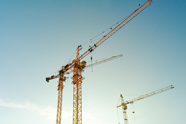 Hoisting construction cranes on construction site against blue sky construction of houses