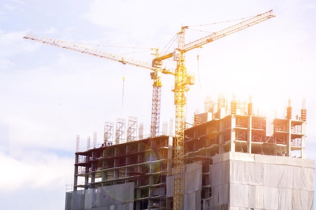 Hoisting cranes working building construction on bright blue sky and big cloud with sun flare