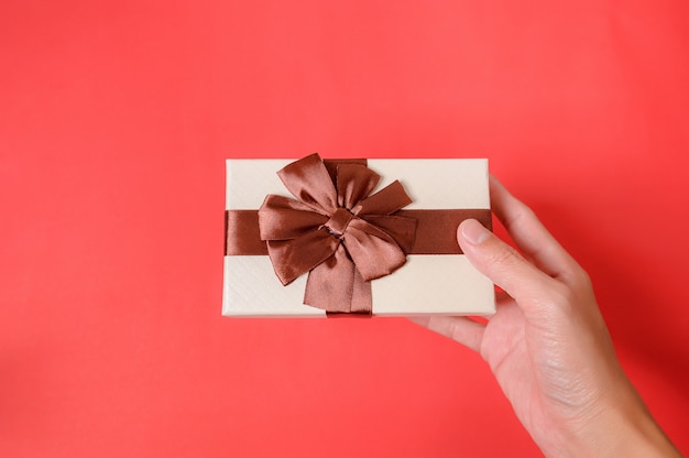 Hold giving gift box on a red background.