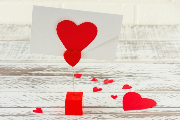 Держатель с конвертом с любовным письмом. Открытка на день Святого Валентина на деревянных фоне. Праздничная открытка с бумажными сердечками.