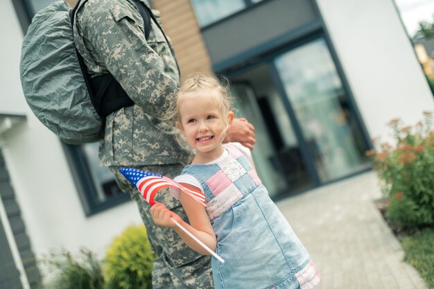 Holding American flag. Lovely girl holding American flag walking home with her hero returning back home