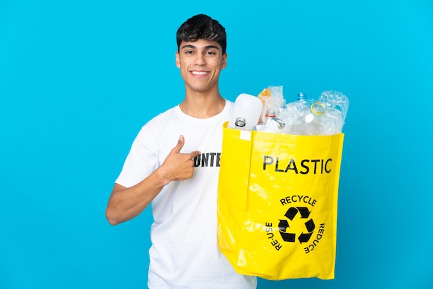 In possesso di un sacchetto pieno di bottiglie di plastica da riciclare su sfondo blu con espressione facciale sorpresa