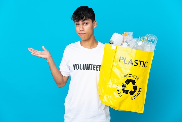 Holding a bag full of plastic bottles to recycle over blue having doubts while raising hands