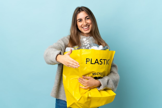 Holding a bag full of plastic bottles to recycle over isolated blue handshaking after good deal