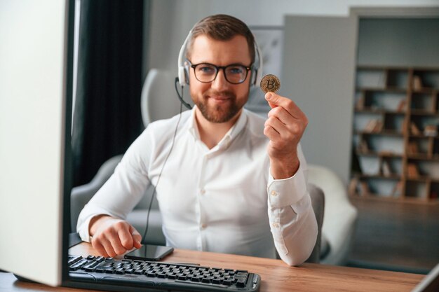 Photo holding bitcoin in the hand man in formal clothes is working in the modern office using computer