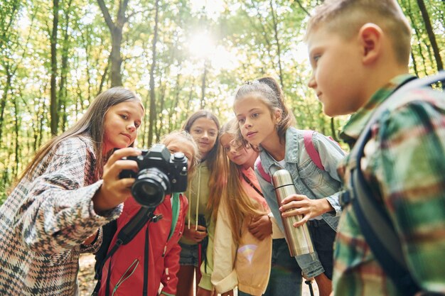 Photo holding camera kids in green forest at summer daytime together