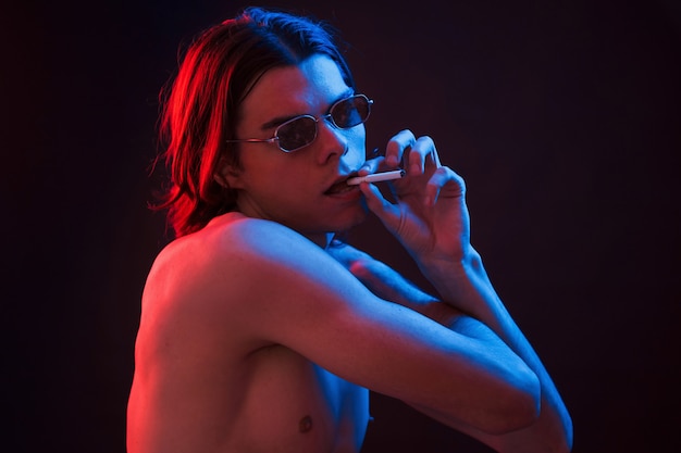 Holding cigarette. Studio shot in dark studio with neon light. Portrait of serious man.