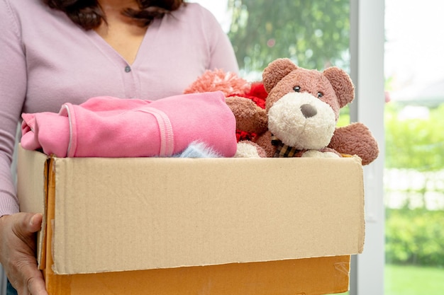 Holding clothing donation box with used clothes and doll at home to support help for poor people in the world