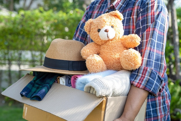 Holding clothing donation box with used clothes and doll at home to support help for poor people in the world.