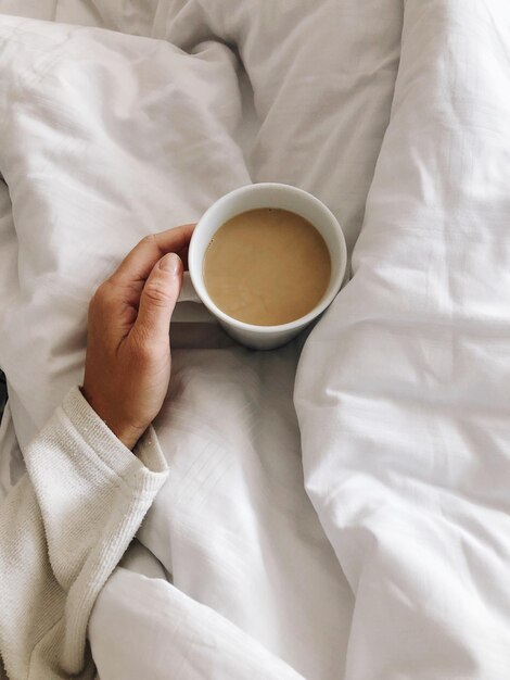 holding a coffeecup in bed