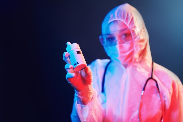 Holding cure pills for coronavirus Nurse in mask and white uniform standing in neon lighted room