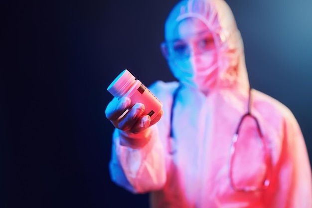 Holding cure pills for coronavirus Nurse in mask and white uniform standing in neon lighted room