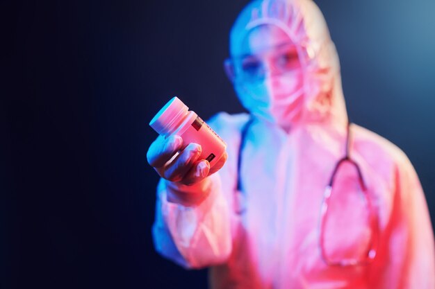 Holding cure pills for coronavirus. Nurse in mask and white uniform standing in neon lighted room