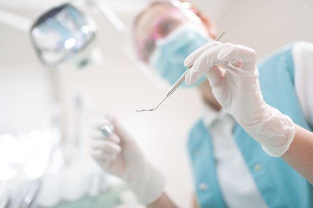 Holding dental equipment. Close up of dentist wearing uniform holding dental equipment while examining patient