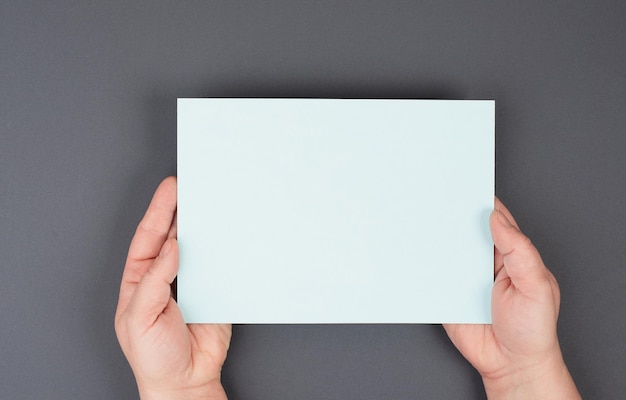 Holding empty paper in the hands, gray colored background, copy space for text, blank card