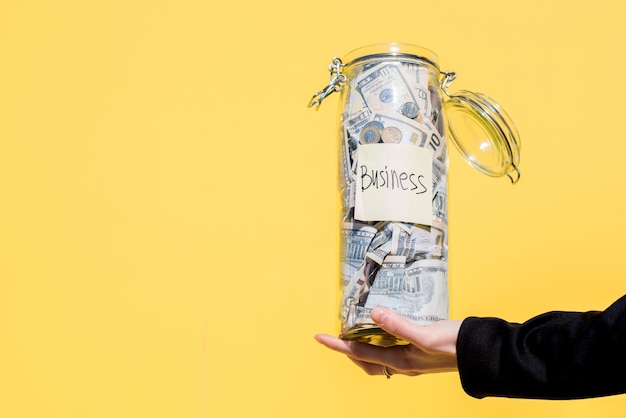 Holding a glass bottle full of money savings for business investment on the yellow background