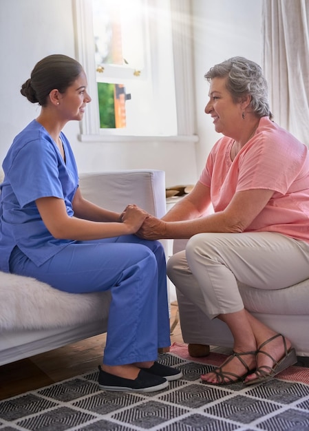 holding hands caregiver and elderly woman on couch with advice for health consulting or compassion lens flare nurse and senior patient for hope trust or medical conversation at retirement home
