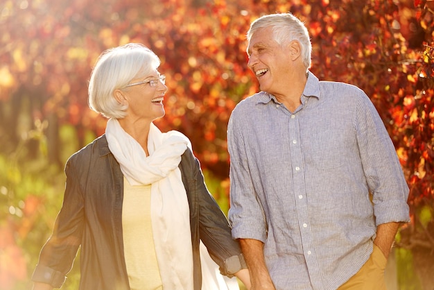 Holding hands laughing and a senior couple in a vineyard walking together while on a romantic date Funny love or romance with a mature man and woman taking a walk on wine farm for bonding