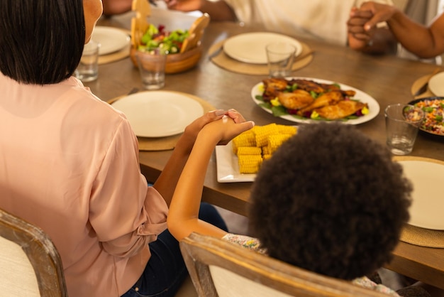 手をつないで一緒に食べる準備をしている食卓に座っている多世代の家族