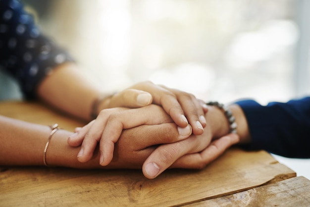 Holding hands support and closeup with trust solidarity and community on a home table Therapy diversity and gratitude of friends together with hope respect and love for grief empathy and forgive