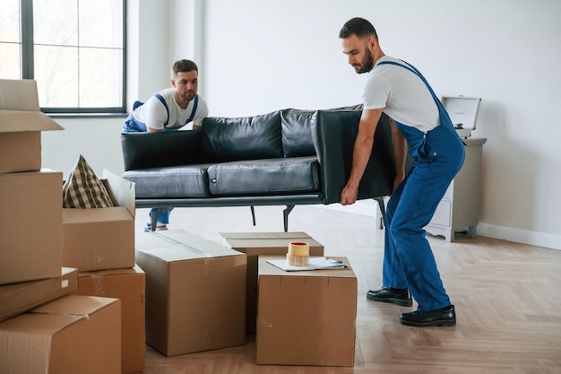 Holding heavy sofa Two moving service employees in a room