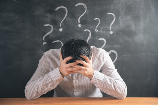 holding his head in his hands and behind a question mark .