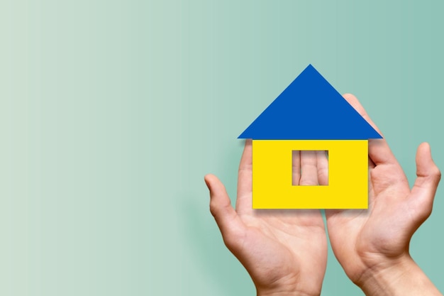 Photo holding a house in the hand with the colors of the ukrainian flag, home for refugees from ukraine,