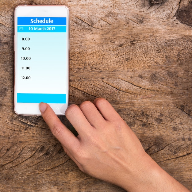 ホームボタンに人差し指を持ち、木製の背景に作業スケジュール