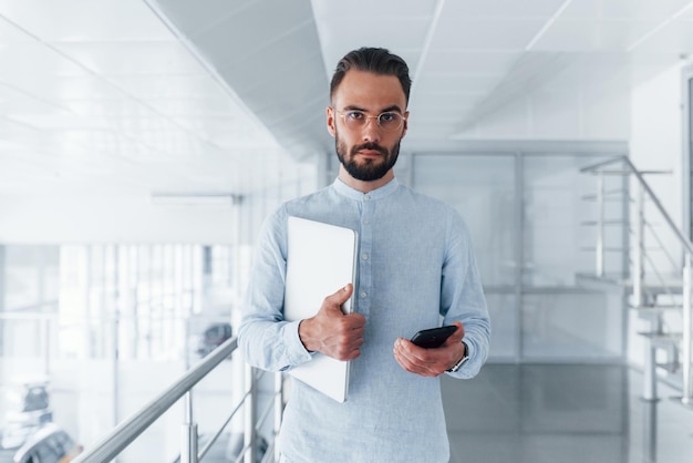 Holding laptop Young handsome man in formal clothes indoors in the office at daytime